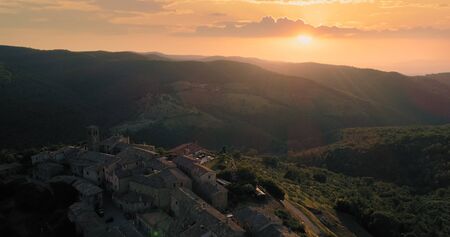 Aerial view flying over rural medieval town or village at sunset or sunrise. Back warm sun light....