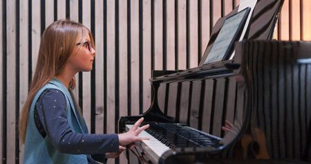 Kid learning to play piano at home.Kid practicing piano.Side view.Little girl playing pianoの写真素材