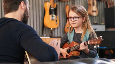 Dad teaching guitar and ukulele to his daughter.Little girl learning guitar at home.Close up.Ukulele class at home. Child learning guitar from her fatherの写真素材