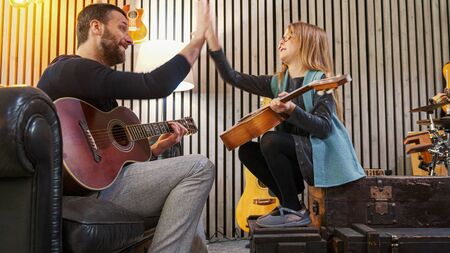 Dad giving five to his daughter celebrating success while teaching music to his daughter.Little girl learning guitar at home.Side view.Ukulele class at home. Child learning guitar from her fatherの写真素材