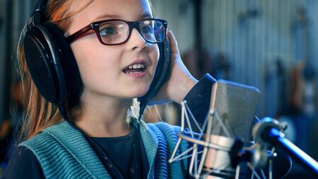 Kid singing in studio.Little girl singing a song.Front view close up. Kid wearing headphones attending singing class.の写真素材