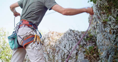 Climber man preparing for climbing up the rocky wall rift by checking rope. Climbing extreme active sport activity. Active people, outdoor activities.Body medium shot.の写真素材