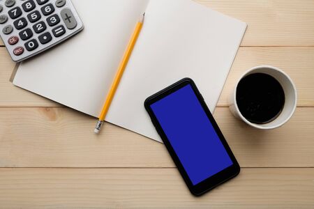 Top view with copy space of wooden working table with calculator, paper cup of hot coffee, yellow pencil, notebook, smartphone.の写真素材