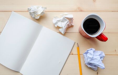 Top view: There are crumpled paper, blank pages of notebook, yellow pencil and hot coffee of red cup on wooden table. For brainstorming, work hard, stress conceptの写真素材