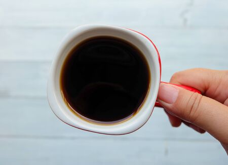 Top view and close up: Sweet milk and strawberry soft cake on wooden plate and a hand is holding a red cup of hot black coffee. Begin of day concept.の写真素材