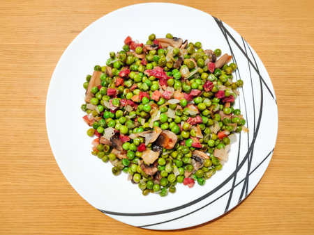 11. Peas with ham, onion and mushrooms as delicious healthy food over white dish and wood tableの写真素材