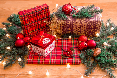 Christmas gifts wrapped and prepared with Christmas tree branches, red balls and warm lightsの写真素材