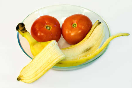Banana and two red tomamos on glass plate on white backgroundの写真素材
