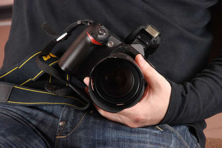 Professional photographer sitting and holding photo camera (digital SLR) in hands closeupの写真素材