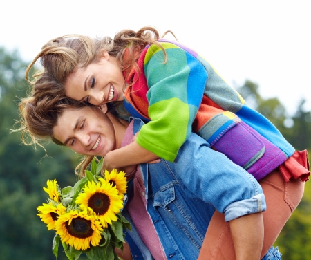 Loving young man hugging his girlfriend with sunflowers in their hands の写真素材