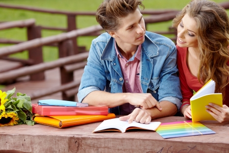 Couple of students holding a notebook outdoors and smiling の写真素材