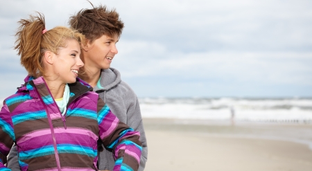 Couple embracing and having fun wearing warm clothes outside on coast behind blue sky の写真素材
