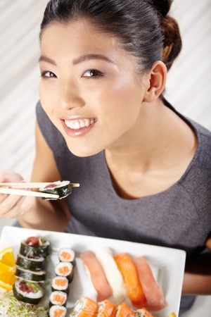 Beautiful young woman eating sushi. Shallow depth of field, focus is on the eyes. の写真素材
