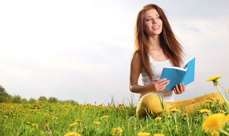 Young beautiful woman on green field and reads book. の写真素材