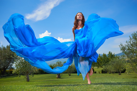 Fashionable beautiful young woman in long blue dress posing with  sky in background.の写真素材