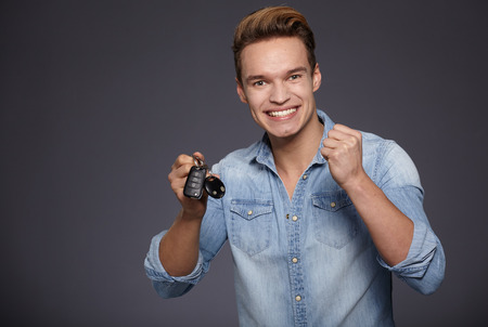 Happy men holding out car keys. Isolated on grey background