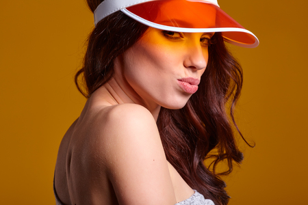 Smiling young woman in orange  sun visor posing in sunlight and looking away. studio shot on yellow background.の写真素材