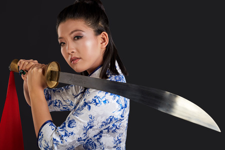 young beautiful Japanese woman looking aggressively at camera and holding swordの写真素材