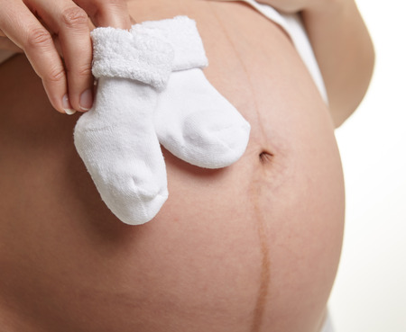 Small shoes for the unborn baby in the belly of pregnant womanの写真素材
