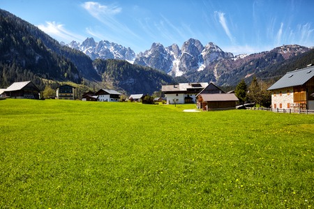Country road leading to the alpine houses, in the background of green meadows and high peaks of the Alpsの写真素材