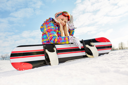 Young female snowboarder sitting on slopeの写真素材