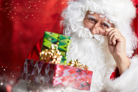 Photo of happy Santa Claus outdoors in snowfall carrying gifts to childrenの写真素材