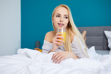 Young beautiful woman with cup of juice in bedの写真素材