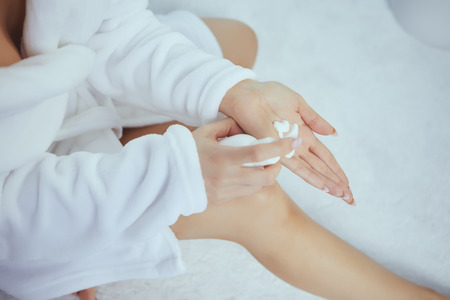Cropped image of beautiful young woman applying hand cream while sitting on bed at hoの写真素材