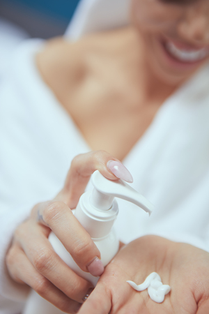 Cropped image of beautiful young woman applying hand cream while sitting on bed at hoの写真素材