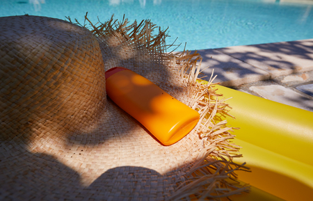 Hat and bottle of sun cream by the poolの写真素材