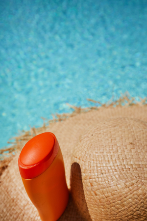 Hat and bottle of sun cream by the pool 