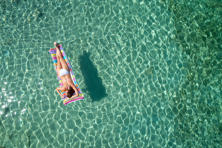 Top view of young woman in a bright bikini is swimming in the transparent, blue sea. Aerial view of...