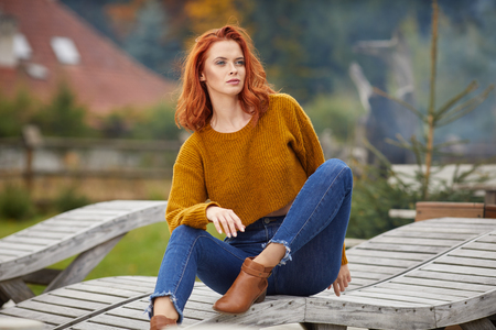 Autumn woman relaxing on a wooden terrace in the morning. Female model with redhairの写真素材