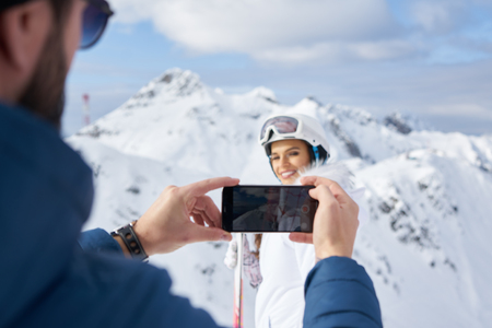 Man Taking Pictures Of His Girlfriend With Smartphone In Winter Stock Photo