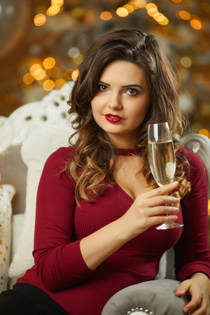 Beautiful girl in evening dress sitting on Christmas decoration  with a glass of wineの写真素材