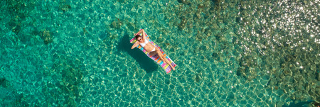 Top down view of a beautiful woman in a white bikini who is floating on a  air mattress