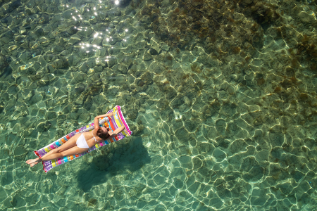 Top down view of a beautiful woman in a white bikini who is floating on a  air mattressの写真素材