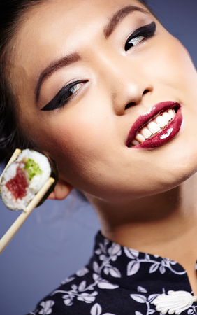 Sushi woman holding sushi with chopsticks looking at the camera smiling.の写真素材