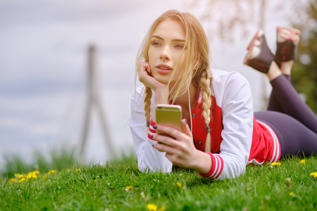 Woman with earphones and smartphone listening to music on grass. In city parkの写真素材
