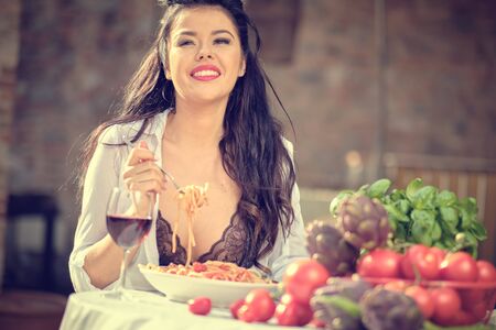 Vintage italian  woman eating italian pasta with tomato sauce and parmesan, served with glass of wineの写真素材