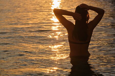 Silhouette of a woman in the sea against the backdrop of the sunsetの写真素材