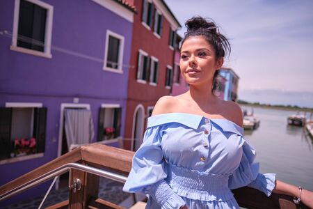 Young fashionable woman in romantic blue  dress  with braid hairstyle, posing near colorful houses...