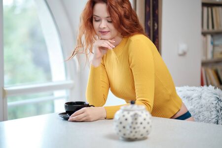 Close up lifestyle portrait of   pensive woman drinking   coffee in early morning, sitting on coach