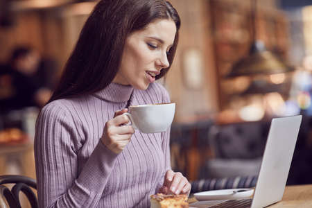 Woman works remotely online from cafe while quarantine coronavirus is in effect. Concept of checking mail, blogger, freelancerの写真素材