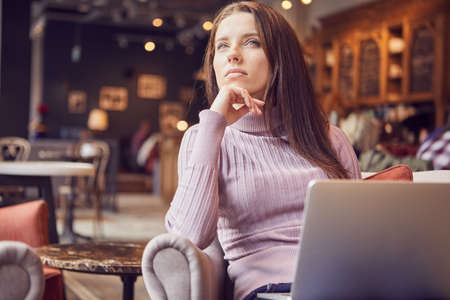 Woman works remotely online from cafe while quarantine coronavirus is in effect. Concept of checking mail, blogger, freelancerの写真素材
