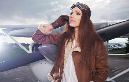 A young female pilot is standing next to a small training planeの写真素材