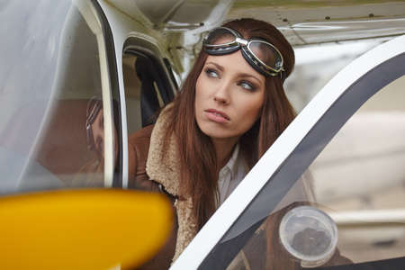 Attractive woman pilot wearing sunglasses standing in the sunshine on an airfield resting against her small private airplaneの写真素材