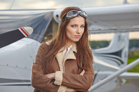 Attractive woman pilot wearing sunglasses standing in the sunshine on an airfield resting against her small private airplaneの写真素材