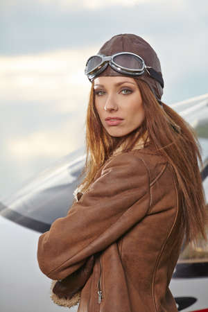 Attractive woman pilot wearing sunglasses standing in the sunshine on an airfield resting against her small private airplaneの写真素材