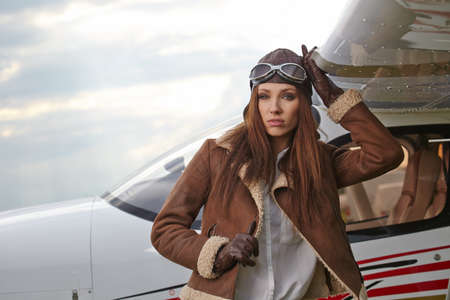 A young female pilot is standing next to a small training planeの写真素材
